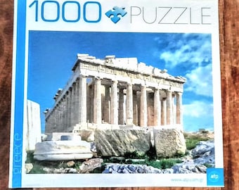 Könnte beinhalten: Ein 1000-Teile-Puzzle mit einem Foto des Parthenon in Athen, Griechenland. Die Schachtel des Puzzles hat einen blauen Hintergrund mit den Worten "1000 Puzzle" und "Griechenland" darauf.