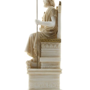 Op de afbeelding: Wit marmeren beeld van Zeus, de Griekse god van de hemel en de donder, zittend op een troon. Hij draagt een kroon van bladeren en houdt een scepter vast. Het beeld staat op een witte marmeren sokkel met gouden accenten.