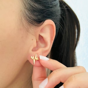 May include: Gold-toned heart beat earrings. The earrings are shaped like a stylized EKG line.