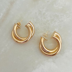 May include: A pair of gold hoop earrings with a double-layered design. The earrings are made of a smooth, shiny metal.