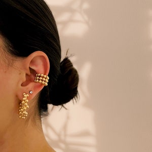 May include: A pair of gold earrings, one is a hoop style with a cluster of small beads, the other is a single row of beads that wraps around the ear.