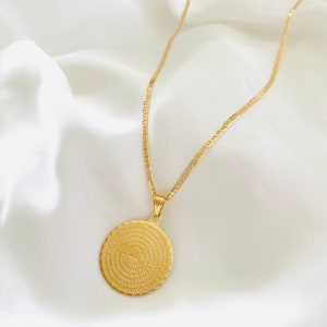 May include: A gold chain necklace with a round pendant featuring a circular inscription in Spanish. The pendant has a textured edge.