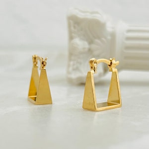 Puede incluir: Un par de pendientes de aro de oro en forma de triángulo. Los pendientes son simples y elegantes.