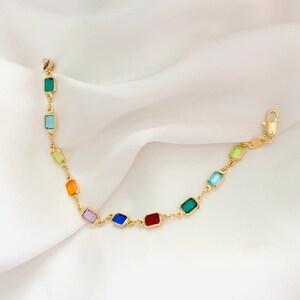 May include: A gold chain bracelet with colorful rectangular gemstones. The gemstones are arranged in a rainbow pattern, starting with green and ending with red.