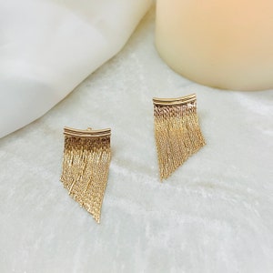 May include: A pair of gold dangle earrings with a fringe design. The earrings are made of a thin chain that hangs down from a curved bar.