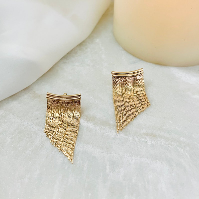 May include: A pair of gold dangle earrings with a fringe design. The earrings are made of a thin chain that hangs down from a curved bar.