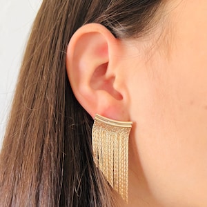 May include: Gold dangle earrings with a fringe design. The earrings are made of a chain-like material and have a curved top.
