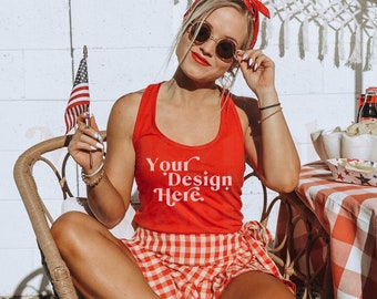 Könnte beinhalten: Eine Frau trägt ein rotes Tanktop mit dem Text "Your Design Here" und sitzt auf einem Korbstuhl mit einem rot-weiß karierten Rock. Sie hält eine kleine amerikanische Flagge und trägt eine Sonnenbrille.