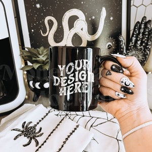 K&ouml;nnte beinhalten: Schwarze Kaffeetasse mit dem Text "YOUR DESIGN HERE" in wei&szlig;en Buchstaben. Die Tasse wird von einer Hand mit schwarz-wei&szlig;em Nagellack gehalten.