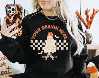 May include: A black sweatshirt with a checkered pattern and a ghost wearing a red hat and riding a skateboard. The text "YOUR DESIGN HERE" is printed on the sweatshirt.