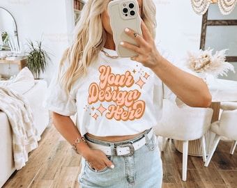 May include: A white t-shirt featuring the text "Your Design Here" in a retro font with orange and pink accents. The shirt is worn with a light blue denim skirt and a white belt.