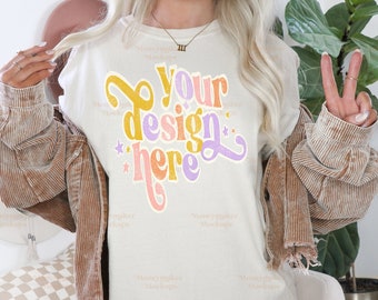 May include: A white t-shirt with a colorful graphic that says "Your design here" with stars around the text. The shirt is being modeled by a person wearing a brown corduroy jacket.