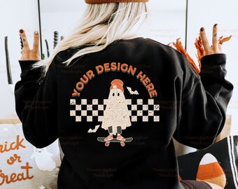 May include: A black sweatshirt with a ghost skateboarding graphic and the text "YOUR DESIGN HERE" printed on the back. The ghost is wearing a red hat and has a checkered pattern behind it.