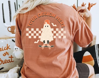 May include: A terracotta colored t-shirt with a ghost skateboarding graphic on the back. The ghost is wearing a red beanie and has a checkered background. The text "YOUR DESIGN HERE" is written in a circle around the ghost.