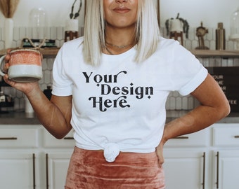 May include: A white t-shirt with the text "Your Design Here" in a black vintage font. The shirt is tied at the waist and the model is holding a light pink and gray ceramic mug.