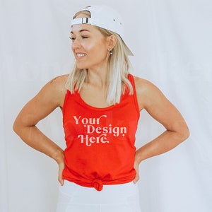 May include: A woman wearing a red tank top with the text "Your Design Here" in white. She is wearing a white baseball cap and white trousers.