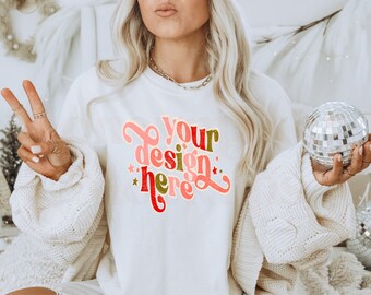 May include: White sweatshirt with the text "your design here" in a retro font with red, pink, and gold accents. The text is surrounded by stars.