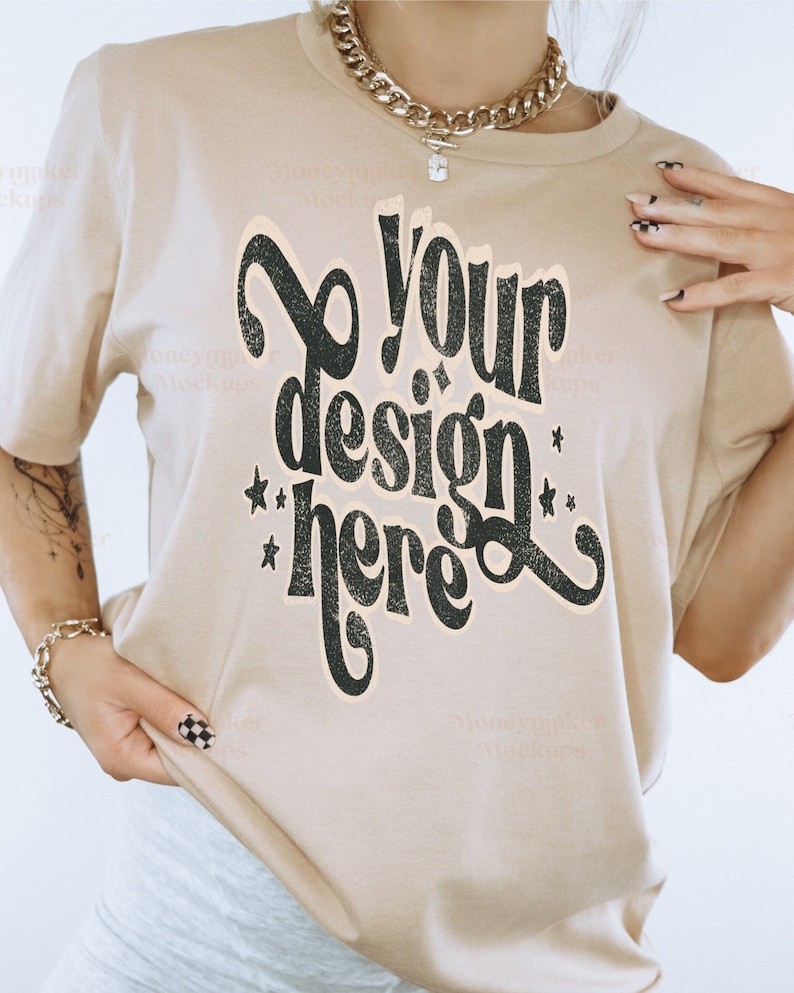Puede incluir: Una camiseta beige con el texto "Your design here" en una fuente retro. La camiseta tiene un corte holgado y mangas cortas.