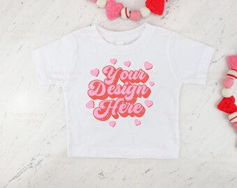 Puede incluir: Camiseta blanca con corazones rosas y rojos y el texto "Your Design Here" en una fuente retro.