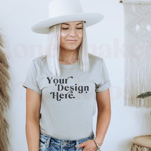 May include: A woman wearing a light gray t-shirt with the text "Your Design Here" in black. She is wearing a white hat and blue jeans.