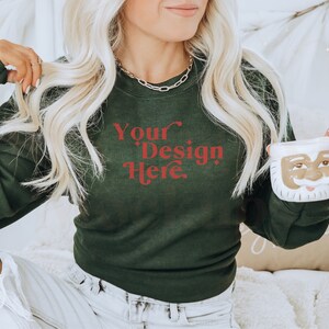May include: A woman wearing a dark green sweatshirt with the text "Your Design Here" in red. She is holding a white ceramic mug with a Santa Claus face.