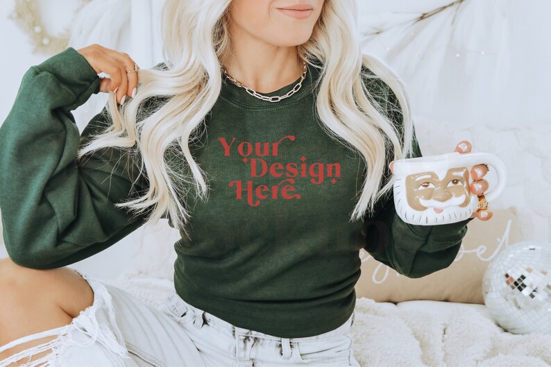 May include: A woman wearing a dark green sweatshirt with the text "Your Design Here" in red. She is holding a white ceramic mug with a Santa Claus face.