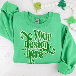 May include: A green sweatshirt with the text "your design here" in a vintage style font. The sweatshirt is folded and laid flat on a white surface.