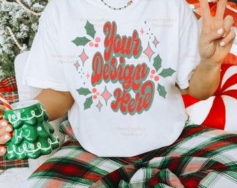 Könnte beinhalten: Ein weißes T-Shirt mit einem grünen und roten Design, auf dem "Your Design Here" steht. Das Shirt wird von einer Person getragen, die auf einer rot-grünen karierten Decke sitzt.