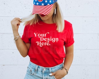 Puede incluir: Una camiseta roja con el texto "Your Design Here" en blanco. La persona lleva una gorra de béisbol azul y blanca y unos vaqueros azules.
