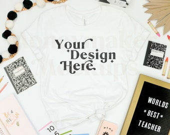 May include: White t-shirt with the text "Your Design Here" in black. The shirt is surrounded by school supplies, including pencils, notebooks, and a letter board that reads "Worlds Best Teacher".