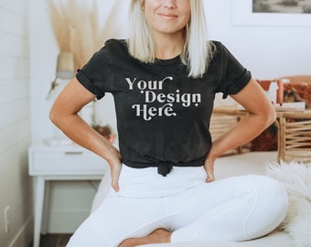May include: A black t-shirt with the text "Your Design Here" in white lettering. The shirt is tied at the waist and the model is wearing white pants.