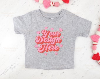 Puede incluir: Una camiseta gris de manga corta con el texto "Your Design Here" en letras rosas y rojas rodeadas de corazones rosas.