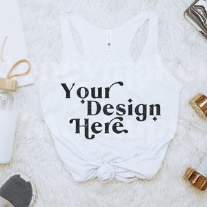 Może przedstawiać: Biały top bez rękaw&oacute;w z napisem "Your Design Here" czarnym pismem jest centralnym punktem tego zdjęcia. Obraz zawiera r&oacute;wnież butelkę wody, hantle, notatnik i trampki, wszystko ułożone na białej, puszystej powierzchni.