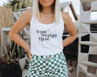 May include: A white tank top with the text "Your Design Here" printed on the front. The tank top is being worn by a person with blonde hair and is paired with green and white checkered shorts.