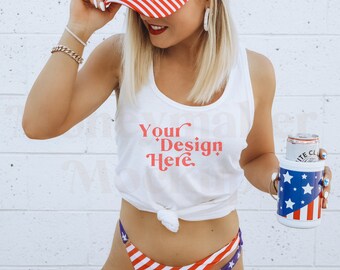 Könnte beinhalten: Ein weißes Tanktop mit dem Text "Your Design Here" in Rot. Das Tanktop ist in der Taille gebunden und das Model trägt einen rot-weiß-blau gestreiften Hut und einen passenden Bikini-Unterteil. Das Model hält einen rot-weiß-blauen Getränkekühler mit einer Bierdose darin.