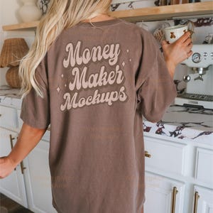 以下が含まれることがあります： レトロなフォントで「Money Maker Mockups」と印刷された、茶色のオーバーサイズTシャツです。