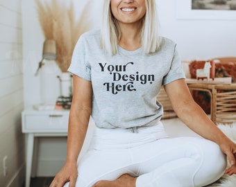 Peut inclure: Une femme portant un t-shirt gris avec le texte "Your Design Here" en noir. Elle est assise les jambes croisées et porte un pantalon blanc.