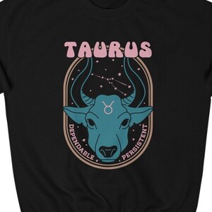 May include: Black sweatshirt with a graphic of a blue bull's head in a circle with the text "Taurus" in pink letters and "Dependable" and "Persistent" written around the circle.