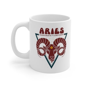 May include: White ceramic mug with a red and blue graphic of an Aries zodiac sign. The text "Aries" is in a retro font and the words "Passionate" and "Confident" are below the sign.