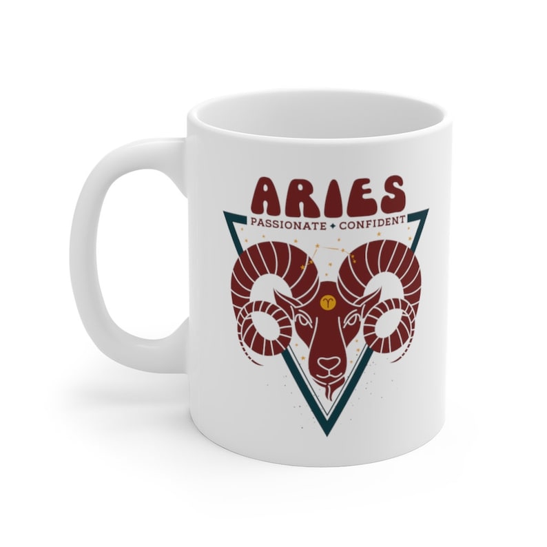 May include: White ceramic mug with a red and blue graphic of an Aries zodiac sign. The text "Aries" is in a retro font and the words "Passionate" and "Confident" are below the sign.