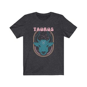 K&ouml;nnte beinhalten: Ein dunkel-helles graues T-Shirt mit einem Grafikdruck eines Bullenkopfes in einem Kreis mit dem Text "Taurus" &uuml;ber dem Bullen und "Dependable" und "Persistent" um den Kreis herum.