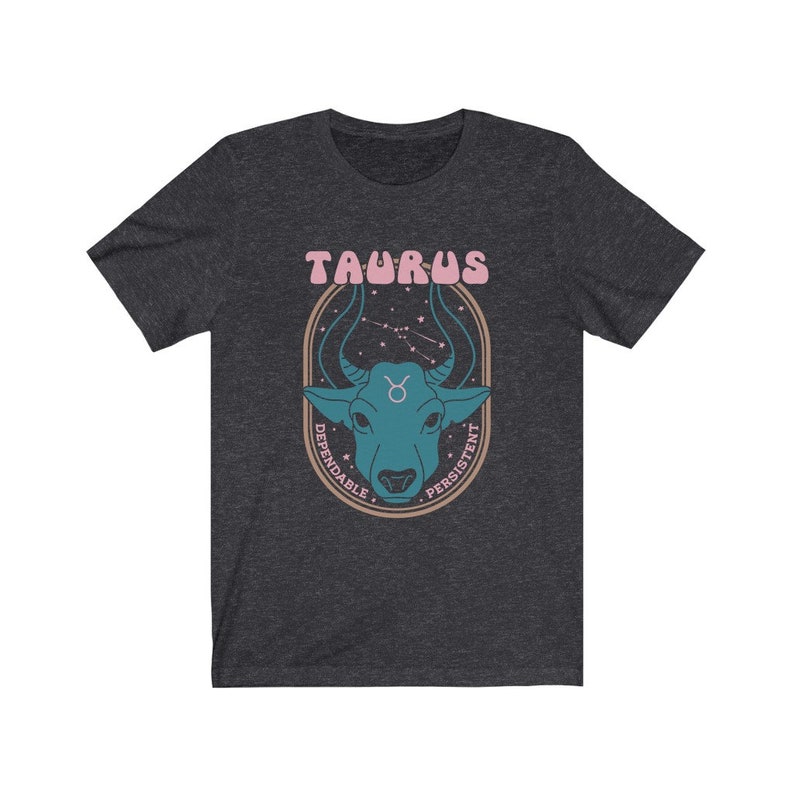 K&ouml;nnte beinhalten: Ein dunkel-helles graues T-Shirt mit einem Grafikdruck eines Bullenkopfes in einem Kreis mit dem Text "Taurus" &uuml;ber dem Bullen und "Dependable" und "Persistent" um den Kreis herum.