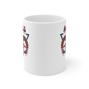 May include: White ceramic mug with a red and blue graphic of a ram's head inside a triangle. The text "Aries" is on the left side of the triangle and "Passionate & Independent" is on the right side of the triangle.