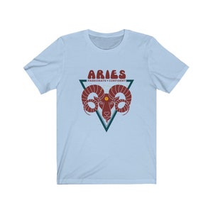 May include: Light blue t-shirt with a red and white graphic of an Aries zodiac sign. The graphic includes the text "Aries" and "Passionate + Confident".