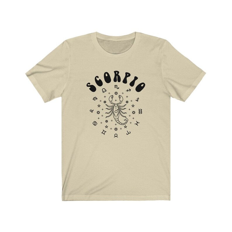 May include: A beige t-shirt with a black graphic of a scorpion surrounded by zodiac symbols and the word "SCORPIO" in a retro font.