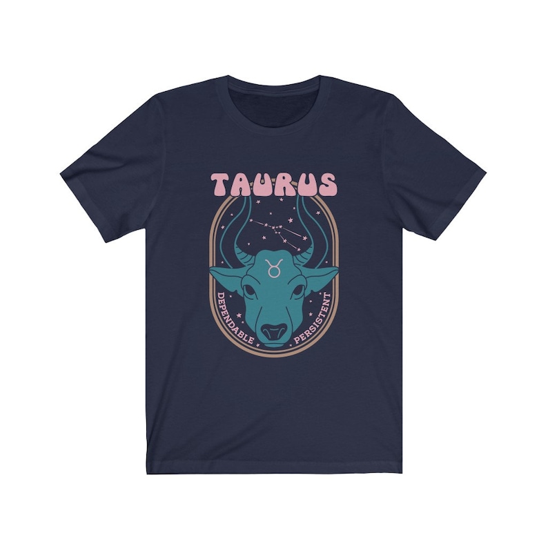 K&ouml;nnte beinhalten: Marineblaues T-Shirt mit einem Grafikdruck eines Stier-Sternzeichen. Das Zeichen ist von einem braunen Kreis umgeben, auf dem die W&ouml;rter "Dependable" und "Persistent" stehen. Die W&ouml;rter "Taurus" stehen in Pink &uuml;ber dem Zeichen.