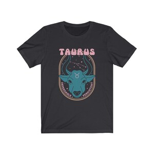 K&ouml;nnte beinhalten: Schwarzes T-Shirt mit einem Grafikdruck eines blauen Bullenkopfes vor einem Hintergrund aus Sternenbildern. Der Text "Taurus" befindet sich &uuml;ber dem Bullenkopf und die W&ouml;rter "Dependable" und "Persistent" sind um den Bullenkopf herum geschrieben.
