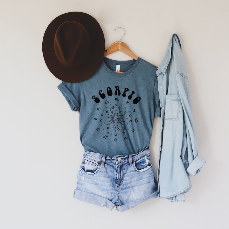 May include: A blue t-shirt with a black graphic of a scorpion and the word "SCORPIO" in a retro font. The scorpion is surrounded by zodiac symbols.