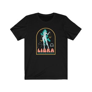 Może przedstawiać: Czarny T-shirt z grafiką kobiety trzymającej wagę, z tekstem "Libra Charming &bull; Diplomatic" pod spodem.