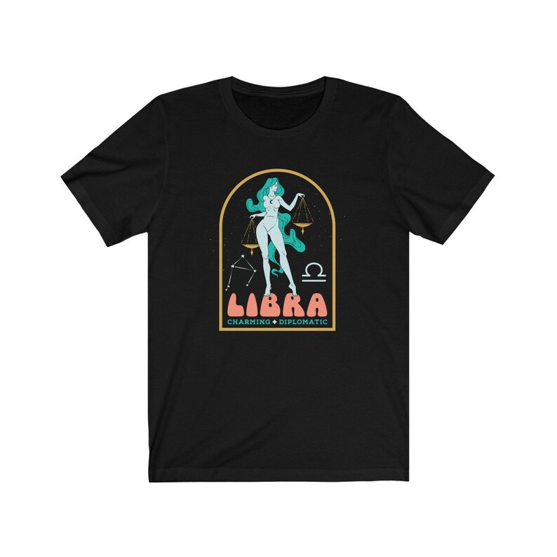 Może przedstawiać: Czarny T-shirt z grafiką kobiety trzymającej wagę, z tekstem "Libra Charming &bull; Diplomatic" pod spodem.